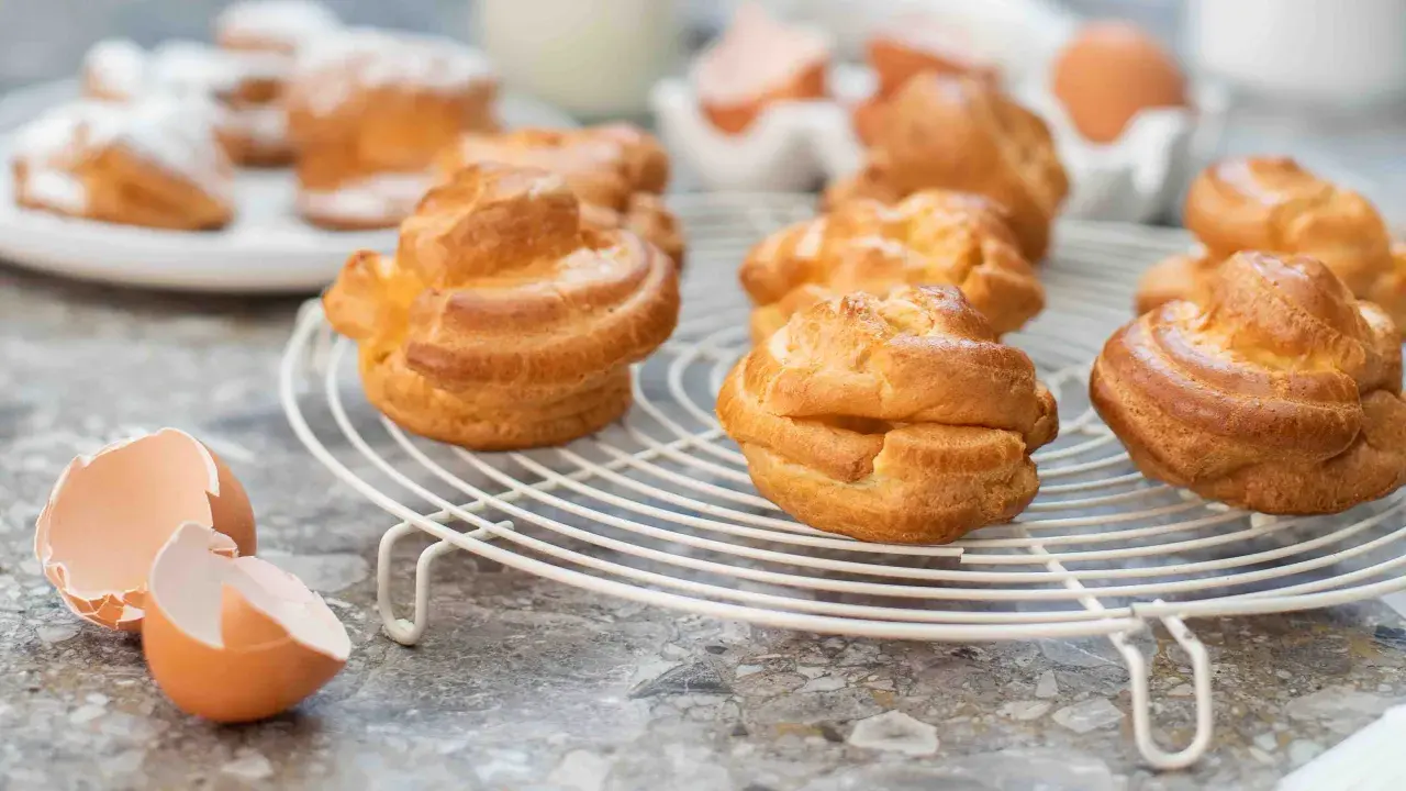 Nybakade petit choux på ett galler, med äggskal i förgrunden. Perfekt för en fika!