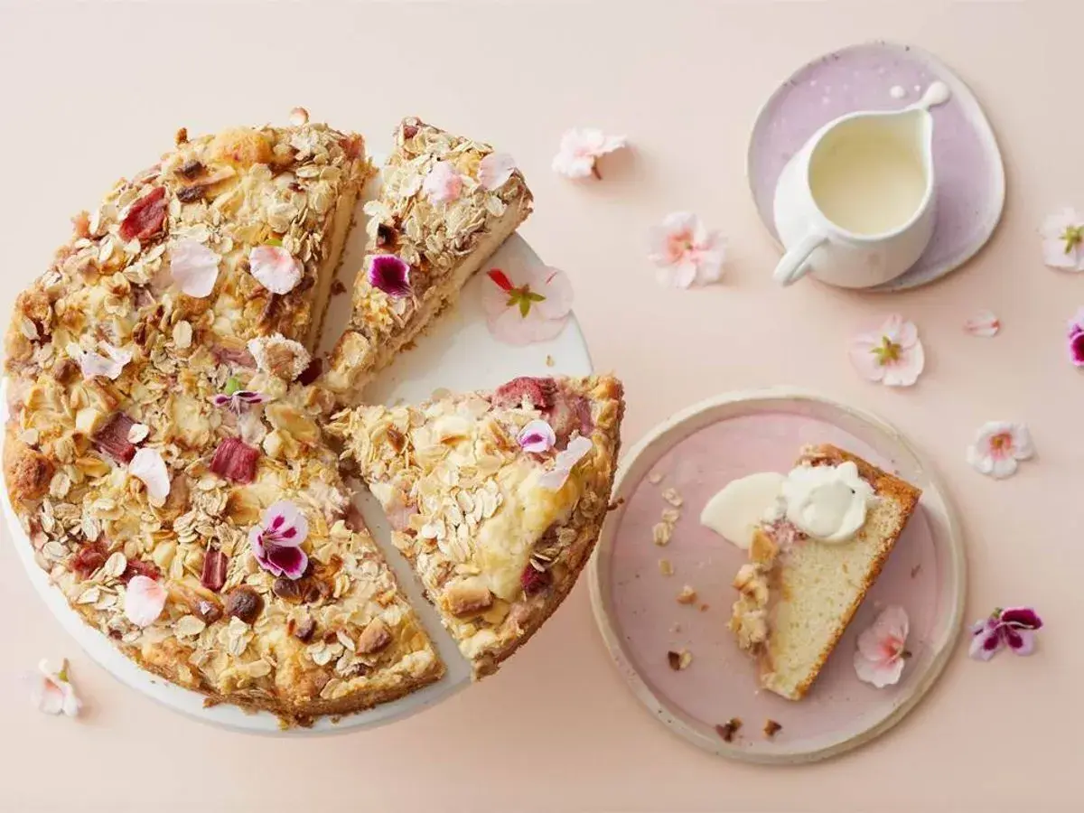 En härlig glutenfri rabarberkaka med havregryn och nötter, dekorerad med blommor. En bit serveras med grädde.