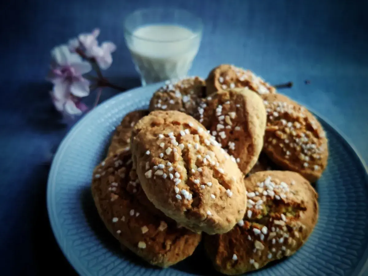 En tallrik med mandelkubbar, toppade med pärlsocker, bredvid ett glas mjölk och en blommande kvist. Perfekt för ett mandelkubb recept.