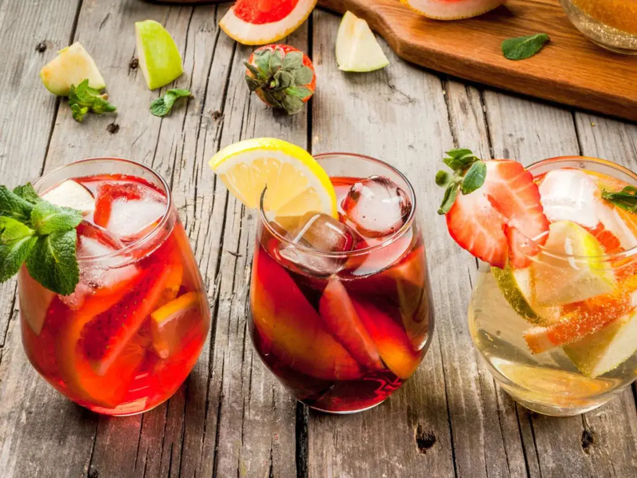 Tre glas med färgglad sangria, fyllda med frukt och is. Perfekt för ett somrigt recept sangria.