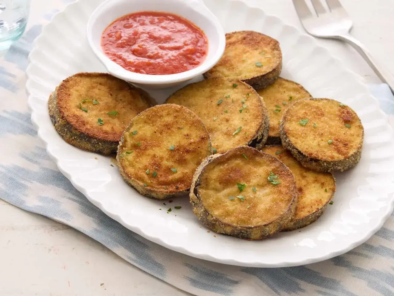 Krispiga skivor av stekt aubergine serveras med en skål tomatsås.