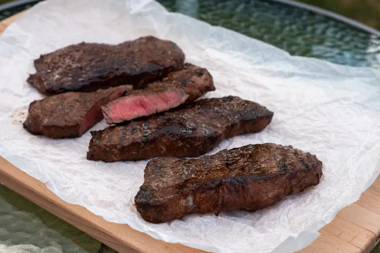Grillad marinad ryggbiff, perfekt rosa i mitten, ligger på bakplåtspapper på en träskärbräda.
