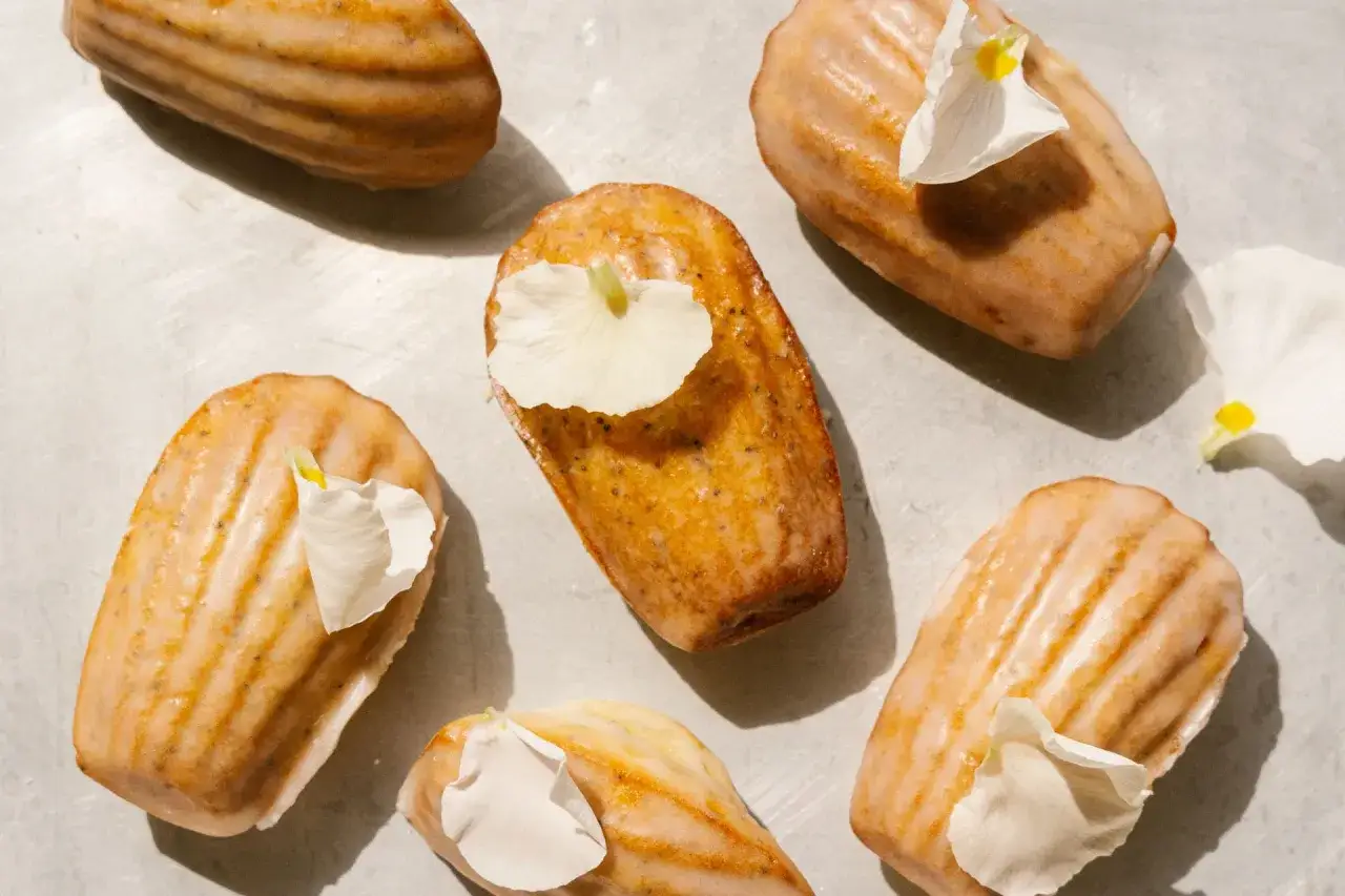Sju gyllene madeleines med en lätt glasyr och vita blomblad. Ett perfekt recept på madeleines för fika.