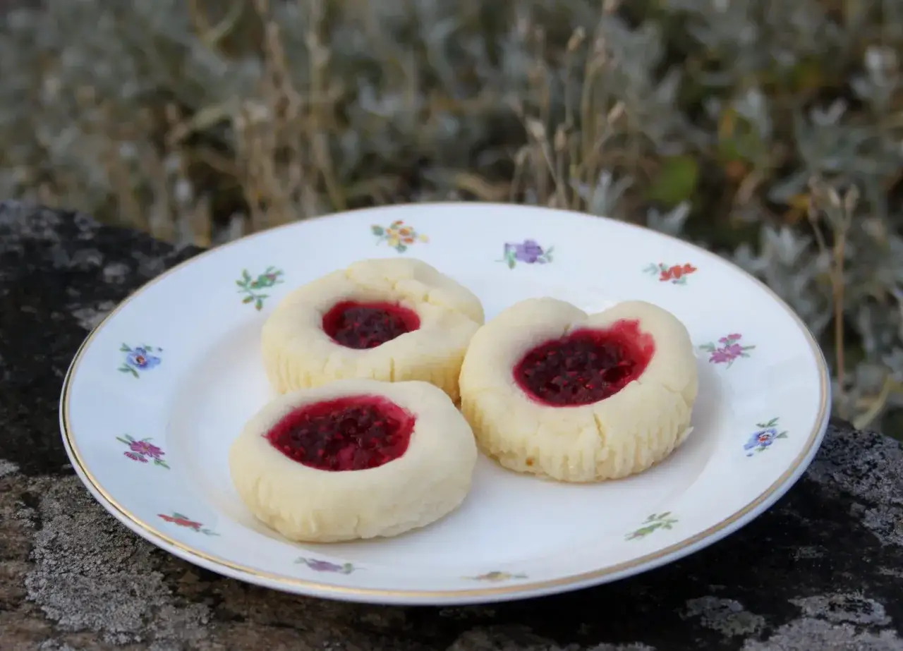 Tre glutenfria hallongrottor med sylt på en blommig tallrik.