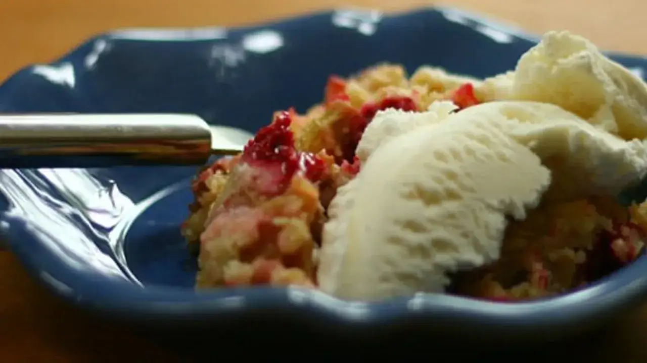 En portion glutenfri rabarberkaka med vaniljglass på en blå tallrik.