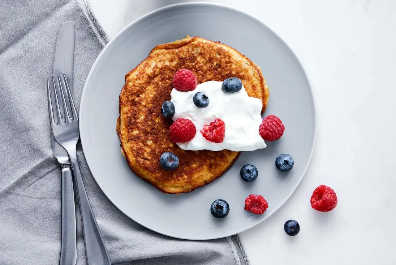 En gyllene bananpannkaka toppad med grädde och bär. Ett perfekt recept på bananpannkaka för en härlig frukost eller mellanmål.