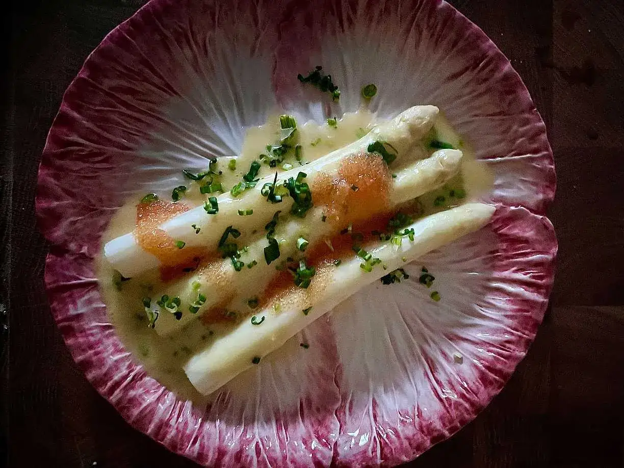 Vit sparris, perfekt blancherad, serveras i en krämig sås med kaviar och gräslök på ett rött endiveblad.
