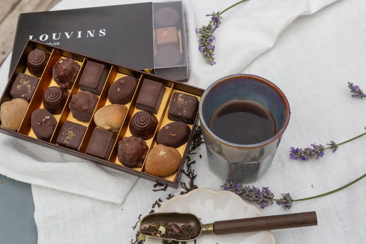En låda med Louvins praliner, perfekt för ett ganache recept till praliner. En kopp kaffe och lavendel fulländar bilden.