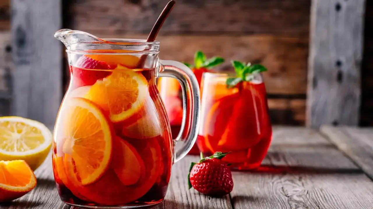 En karaff med sangria fylld med apelsin- och jordgubbsbitar. Ett glas sangria med mynta i bakgrunden. Ett perfekt recept sangria f&ouml;r sommaren.