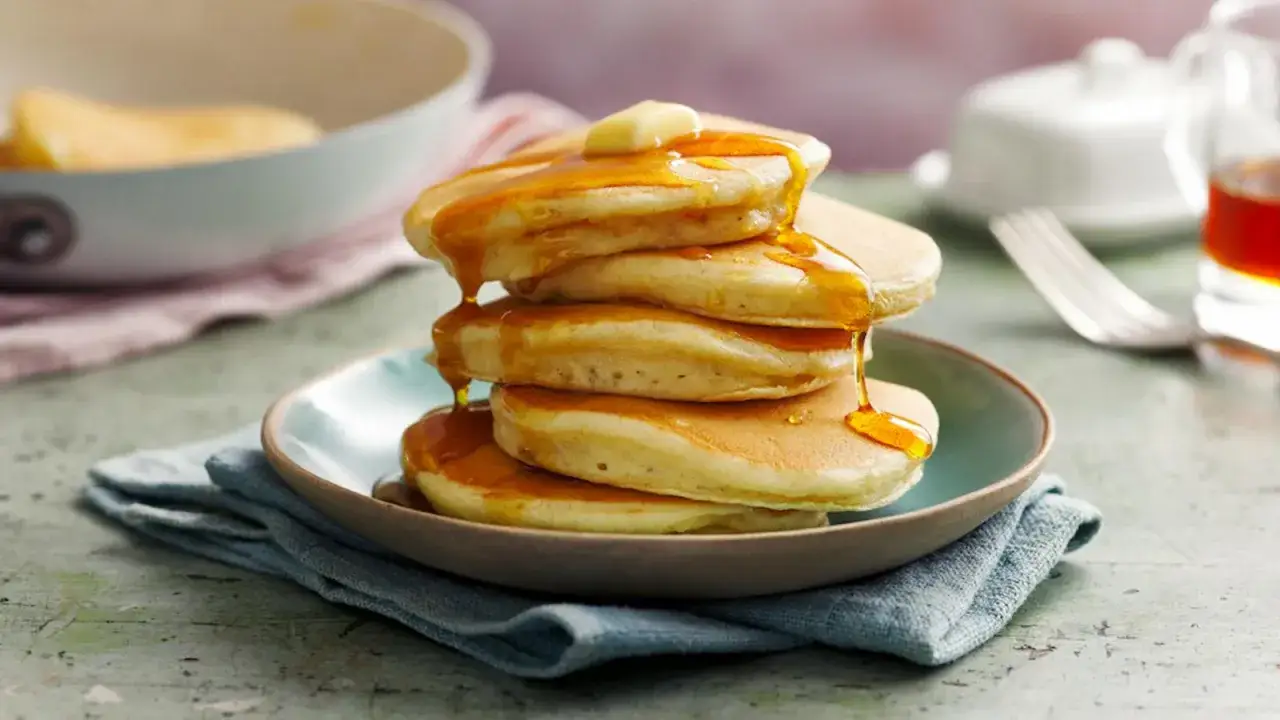En hög med fluffiga amerikanska pannkakor, toppad med smör och sirap. Perfekt för ett amerikanskt pannkakor recept!