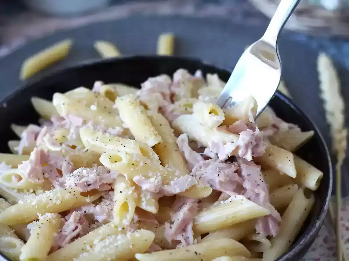 Enkel pastasås med penne, skinka och parmesan. En gaffel lyfter en portion av denna krämiga och smakrika rätt.