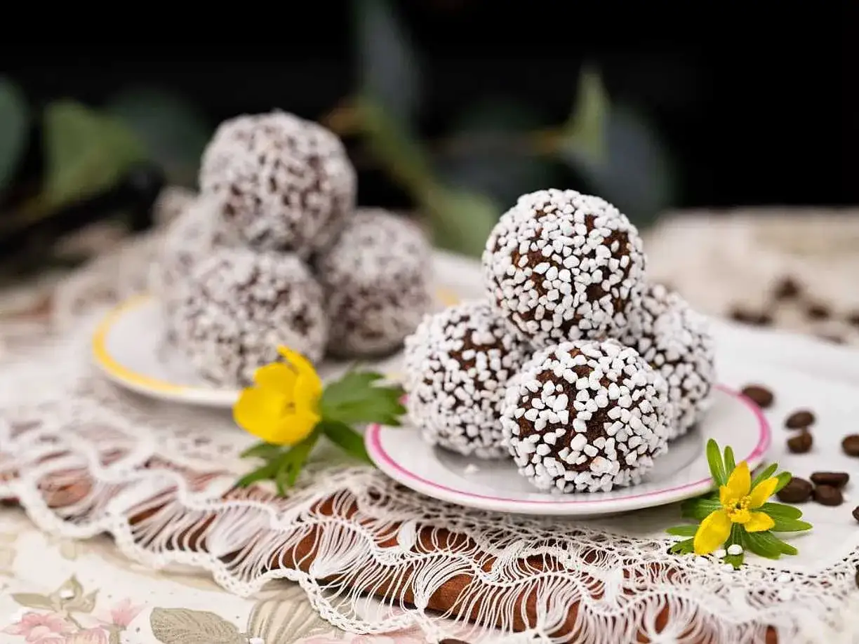Chokladbollar recept: Mumsiga chokladbollar rullade i pärlsocker, vackert upplagda på fat med gula blommor och kaffebönor.