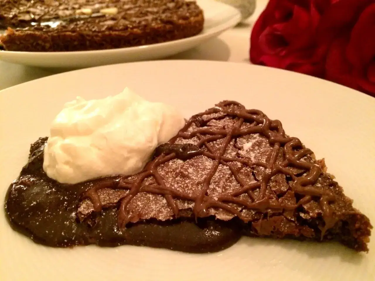 En bit kladdkaka med nutella, pudrad med florsocker och garnerad med chokladdrizzle, serveras med en klick vispad grädde.