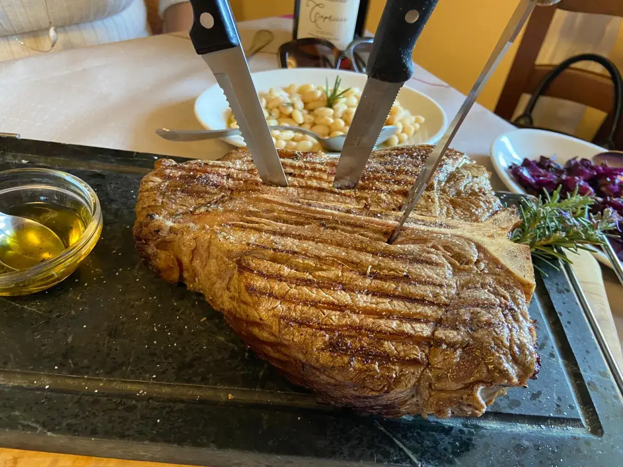 En perfekt grillad bistecca fiorentina med rosmarin och olivolja. Knivar sticker upp ur k&ouml;ttet, redo att sk&auml;ras.