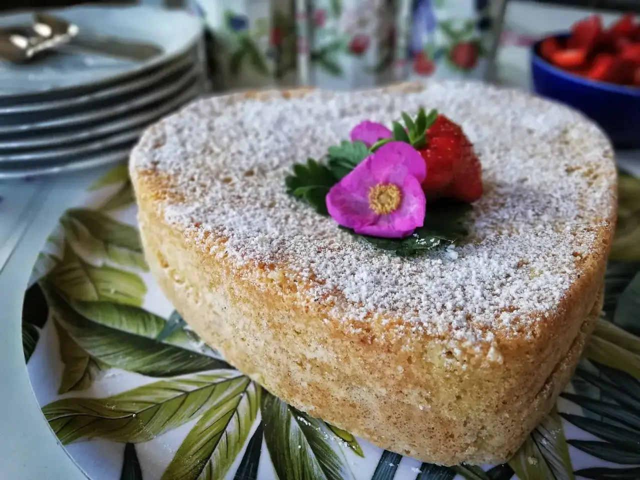 Hjärtformad sverige kaka med florsocker, jordgubbar och en rosa blomma. Perfekt för fika.
