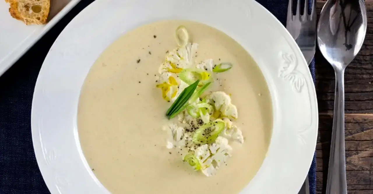 Krämig potatis och blomkålssoppa med toppning av blomkålsbuketter och salladslök. Serveras med en bit rostat bröd.