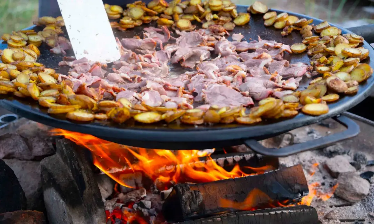 K&ouml;tt och potatis steks p&aring; en muurikka &ouml;ver &ouml;ppen eld. Ett perfekt recept f&ouml;r utomhusmatlagning.