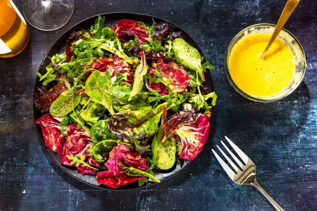En fräsch sallad med blandade gröna blad och röd radicchio, serverad med en krämig dressing till sallad. En gaffel och en skål med dressing syns bredvid.