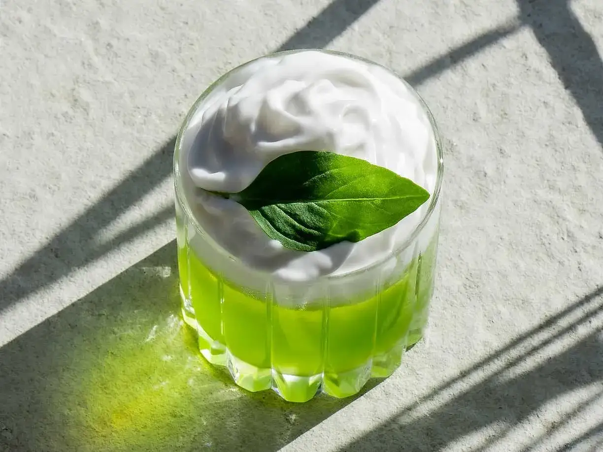 En gr&ouml;n, uppfriskande thai basil drink med ett fluffigt vitt t&auml;cke och ett gr&ouml;nt blad.