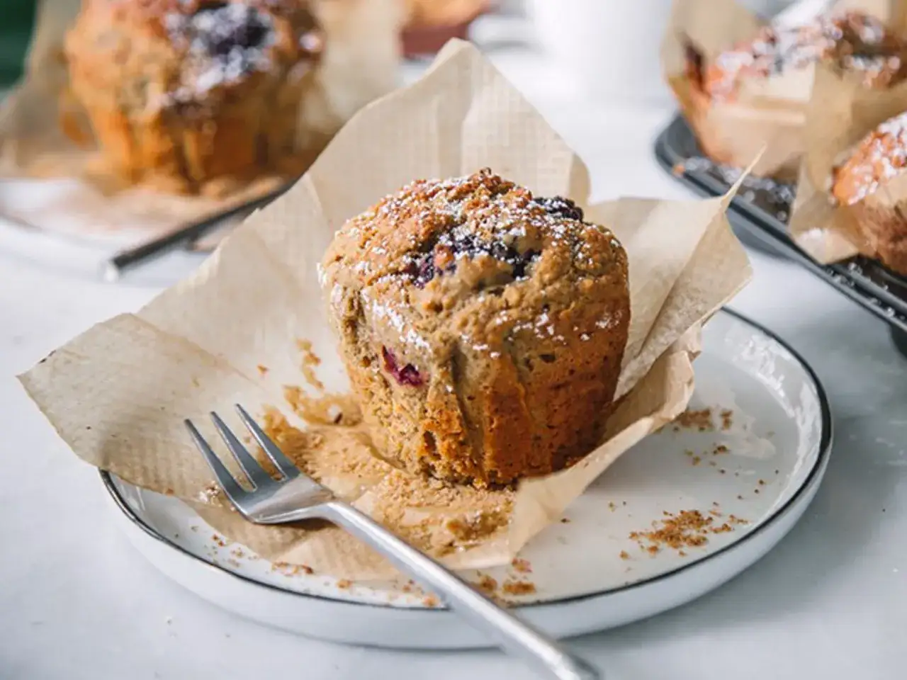 En närbild på en nybakad muffin med bär, pudrad med florsocker. Perfekt för ett enkelt muffins recept.