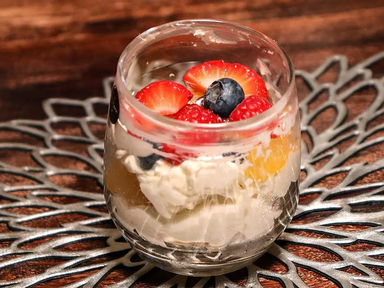 En glasdessert med lager av krämig citron cheesecake, färska bär som jordgubbar, hallon och blåbär, samt bitar av aprikos.