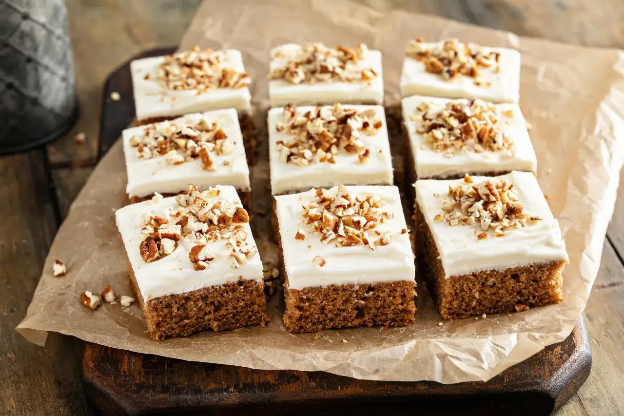 Nio bitar saftig morotskaka i långpanna med krämig frosting och hackade nötter, redo att avnjutas.