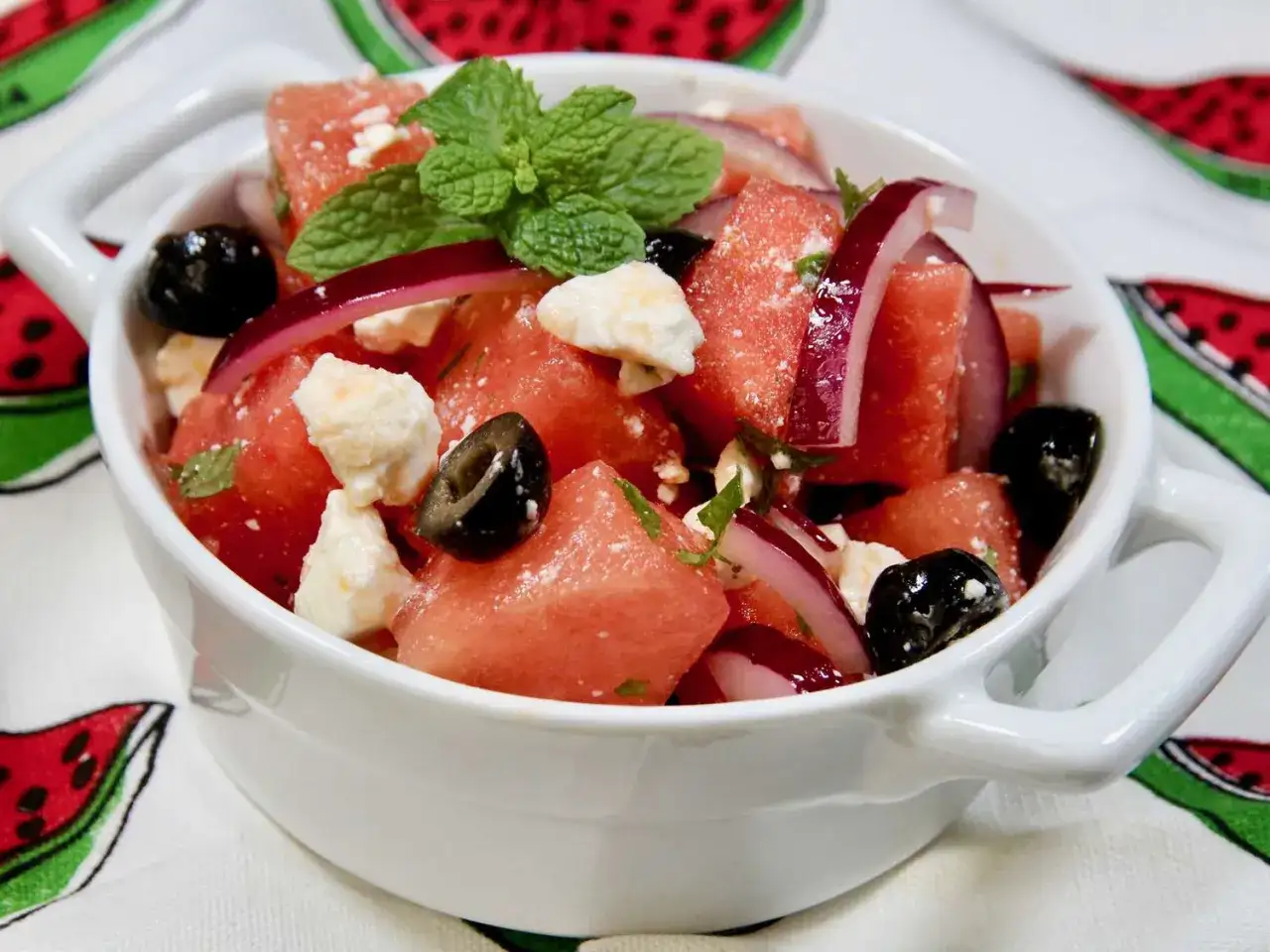 En uppfriskande melon och fetaostsallad med svarta oliver och mynta, serverad i en vit skål.