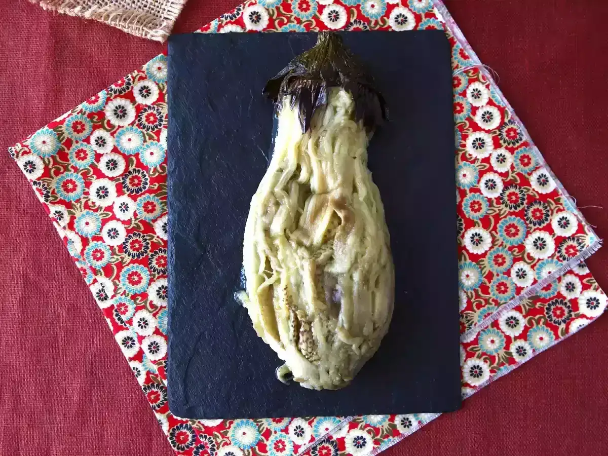 En ugnsbakad aubergine, mjuk och saftig, serverad på en svart skifferplatta.