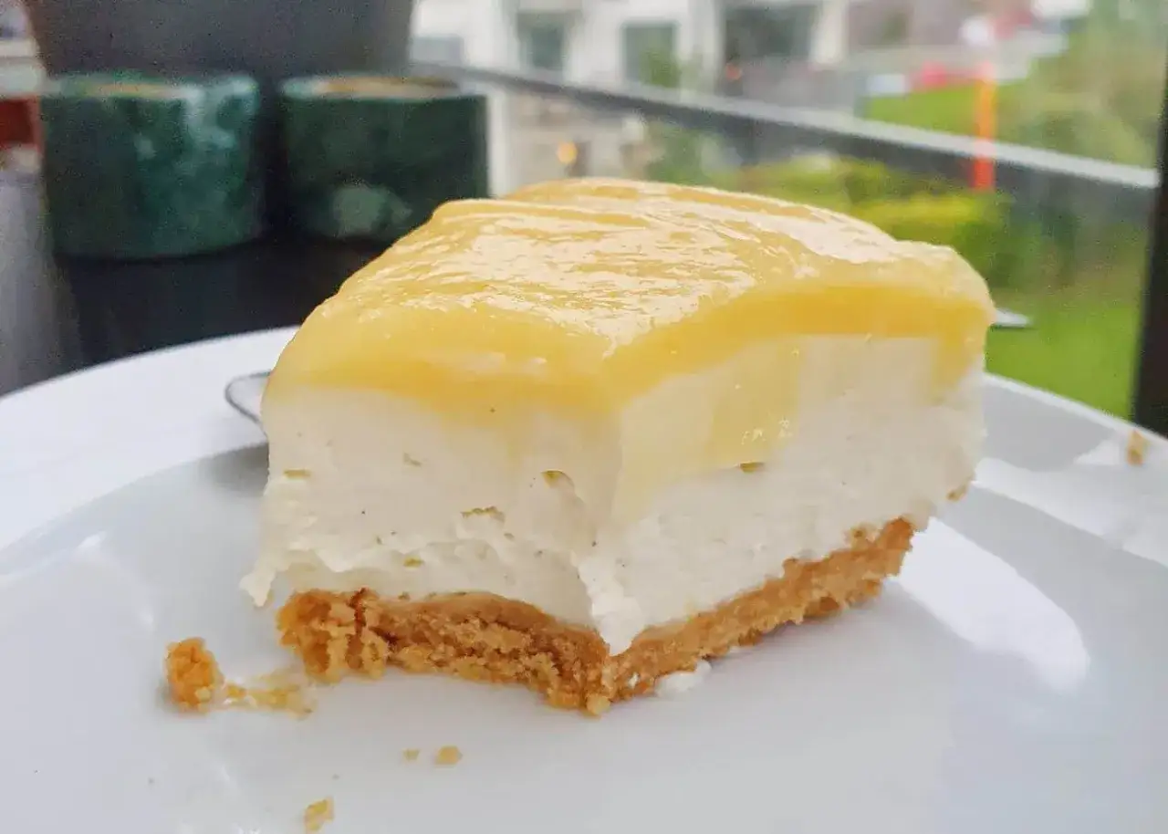En bit krämig cheesecake med kexbotten och en glansig citron frosting.