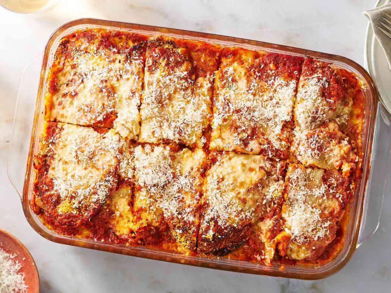 En ugnsform med en gyllene, bubblande melanzane alla parmigiana, toppad med riven parmesan.