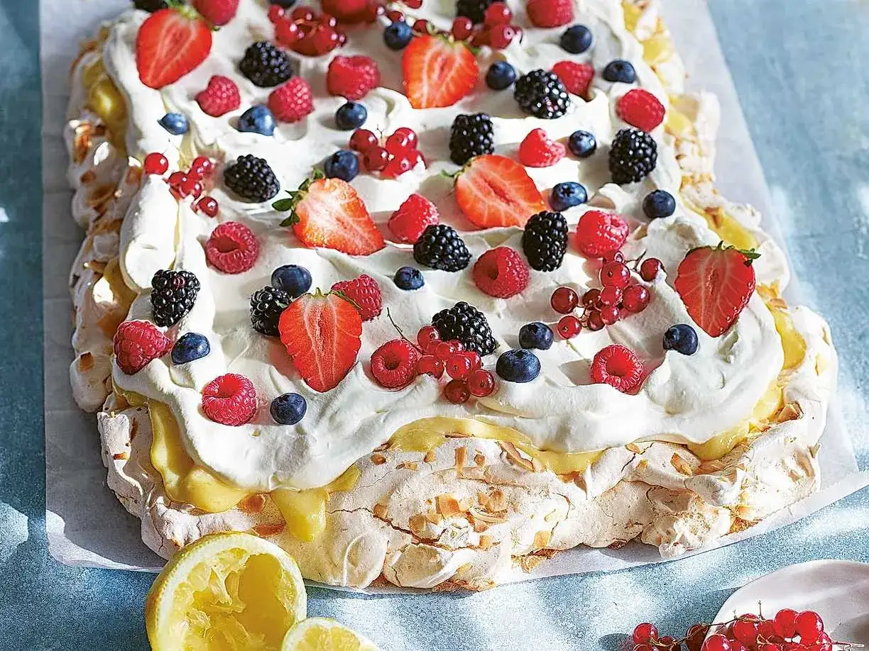 En stor pavlova med lemoncurd, toppad med vispgrädde och färska bär som jordgubbar, hallon, blåbär och vinbär.
