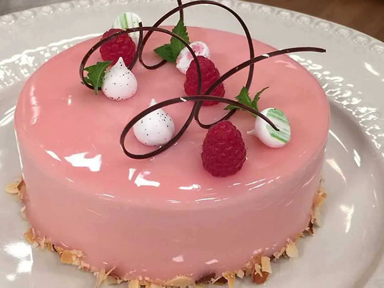 En rosa tårta med hallon frosting, dekorerad med färska hallon, marängtoppar och chokladspiraler.