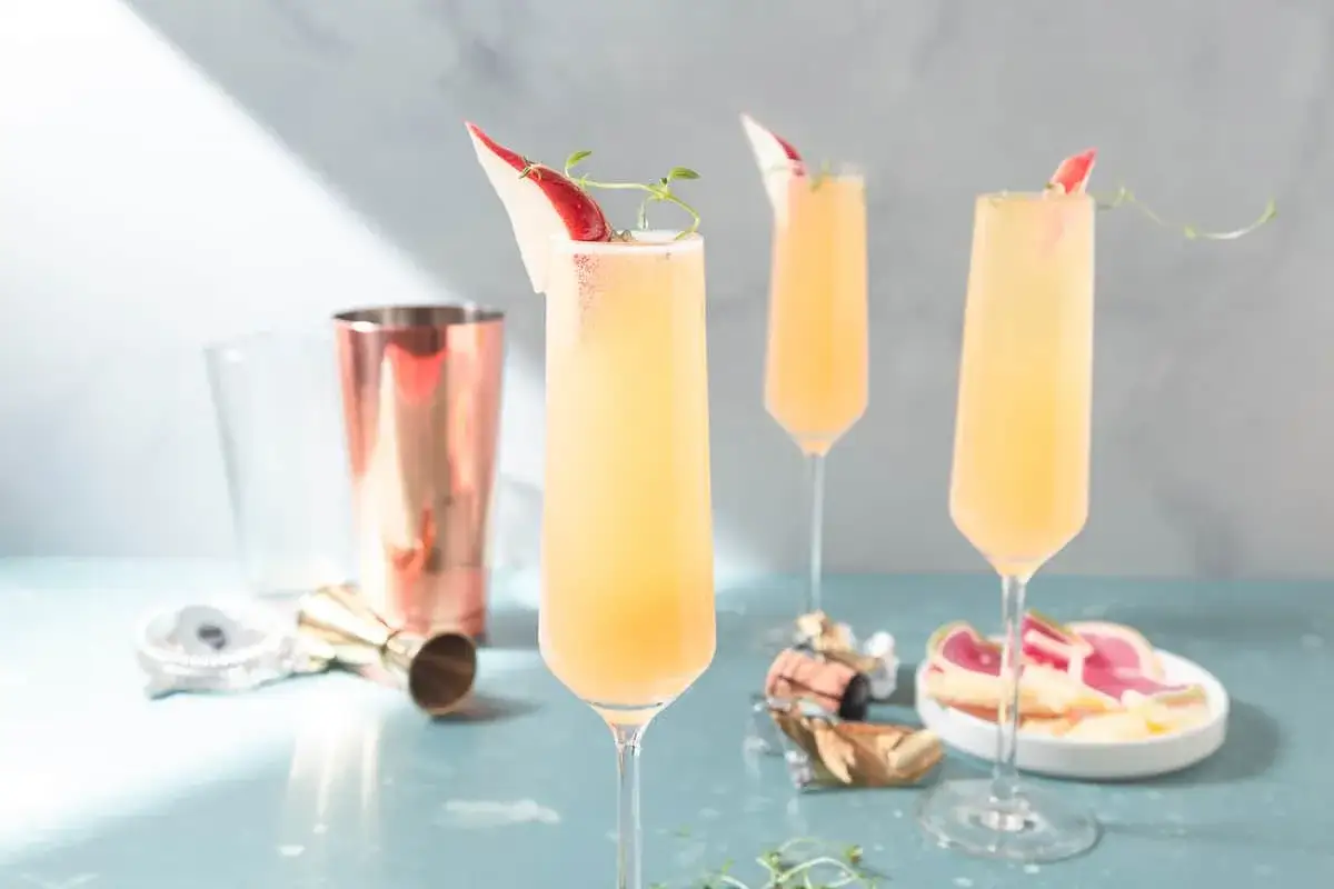 Tre eleganta glas med en uppfriskande drink med gin och prosecco, garnerade med en tunn skiva frukt och en kvist örter.