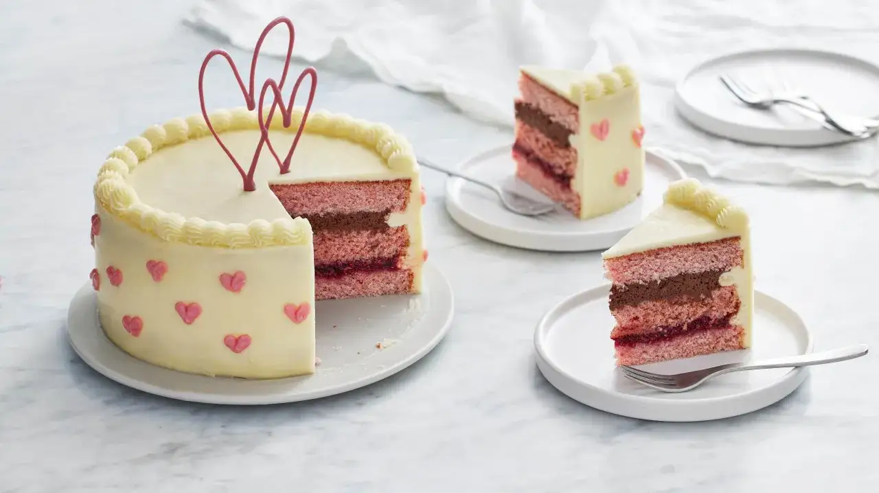 En rosa t&aring;rta med vit frosting, dekorerad med hj&auml;rtan. Skivor visar lager av rosa t&aring;rtbotten, choklad och b&auml;r. Perfekt f&ouml;r enkla t&aring;rtfyllningar.