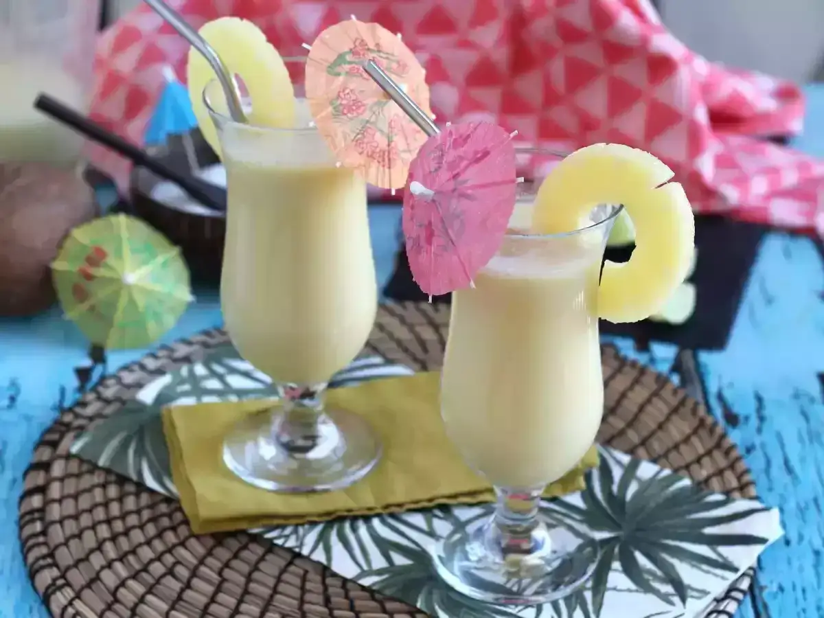 Två glas med krämig, alkoholfri pina colada, dekorerade med ananasskivor och färgglada paraplyer. Perfekt för en tropisk stund.