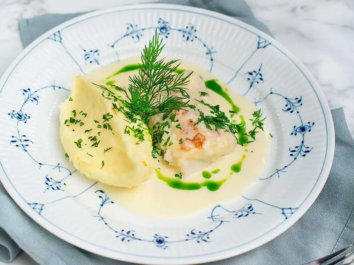 En portion torsk med citronsås, serverad med krämigt potatismos och dill.