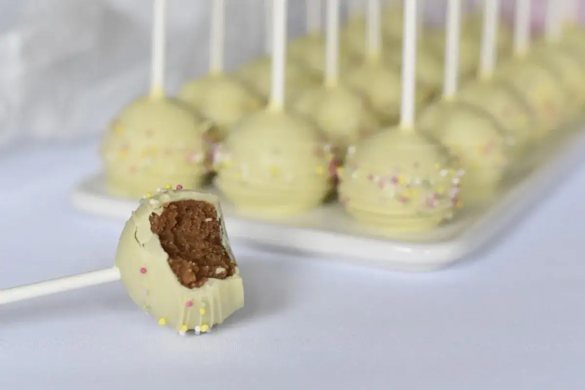En rad med vita cake pops med strössel. En är uppäten och visar det bruna inkråmet.