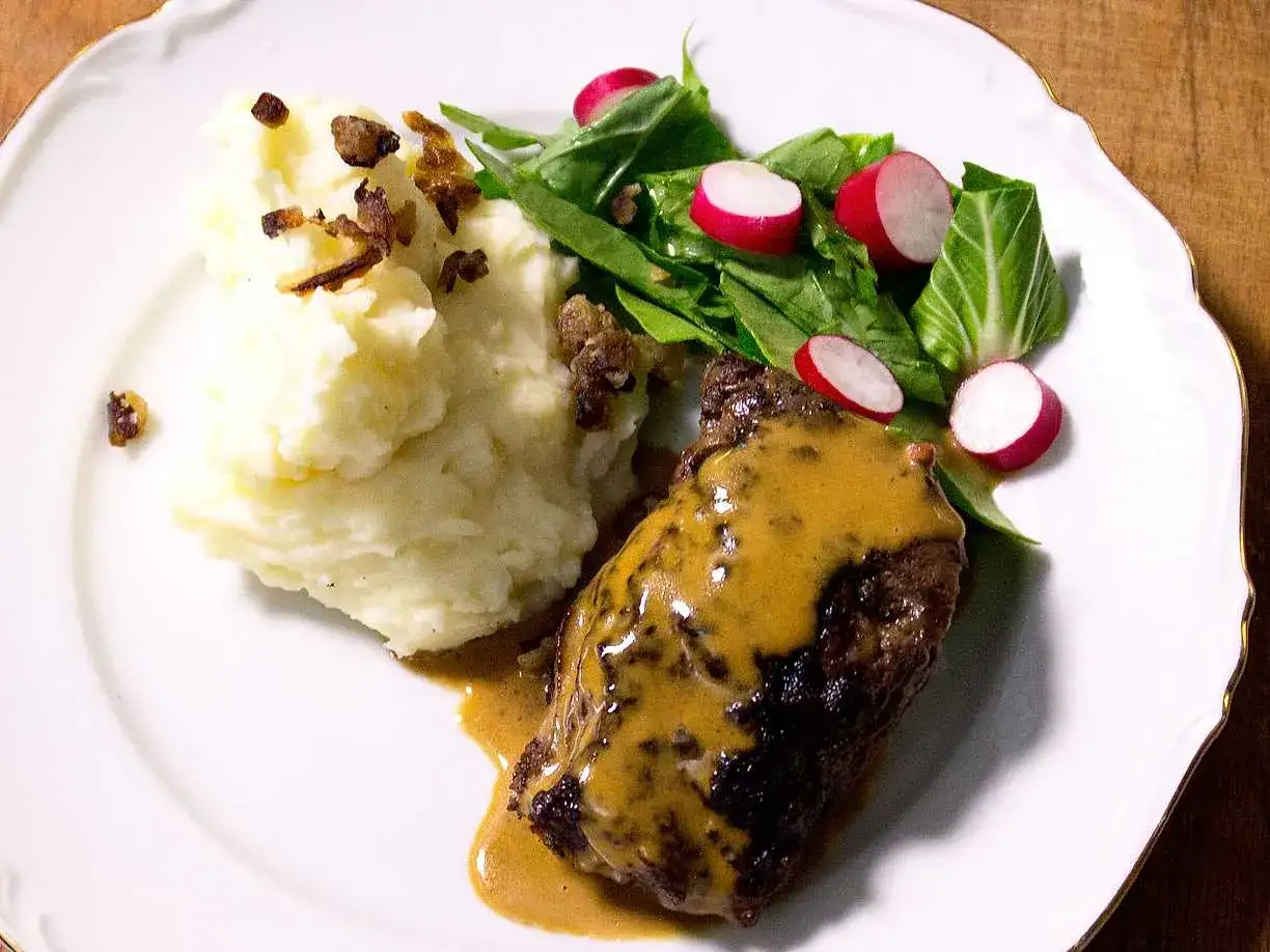 En saftig biff täckt av krämig bbq sås, serverad med fluffigt potatismos och en fräsch sallad med rädisor.