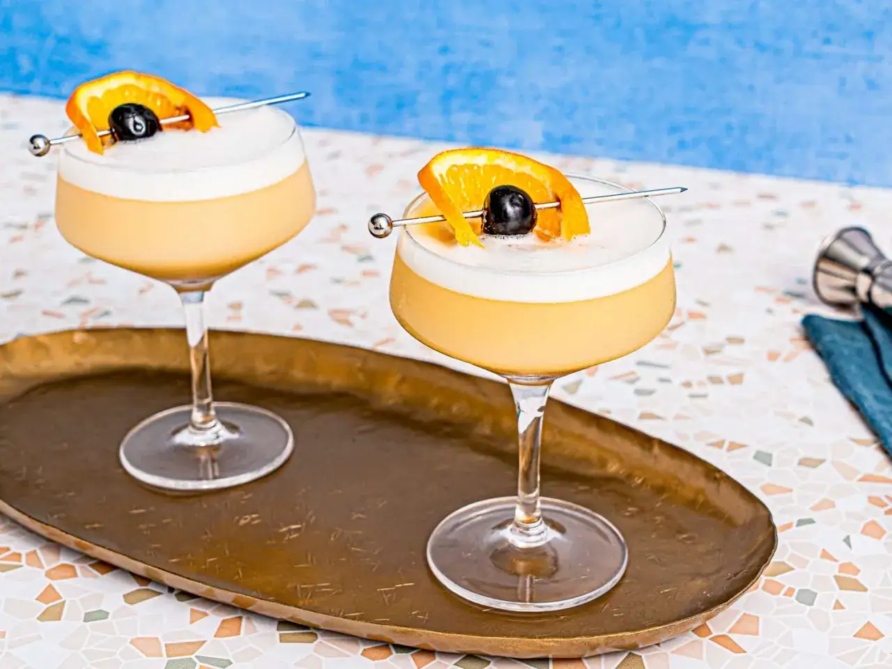 Tv&aring; glas med kr&auml;mig whiskey sour, garnerade med apelsinskiva och k&ouml;rsb&auml;r. Perfekt f&ouml;r en solig eftermiddag.