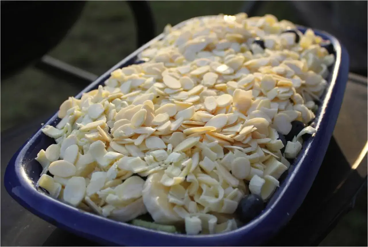 En blå form fylld med frukt och toppad med mandelspån, redo för ett Gino recept.