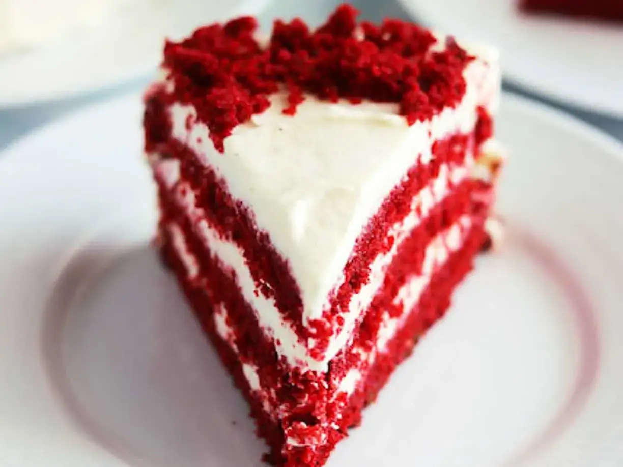 En bit saftig red velvet cake med krämig frosting och smulor på toppen.