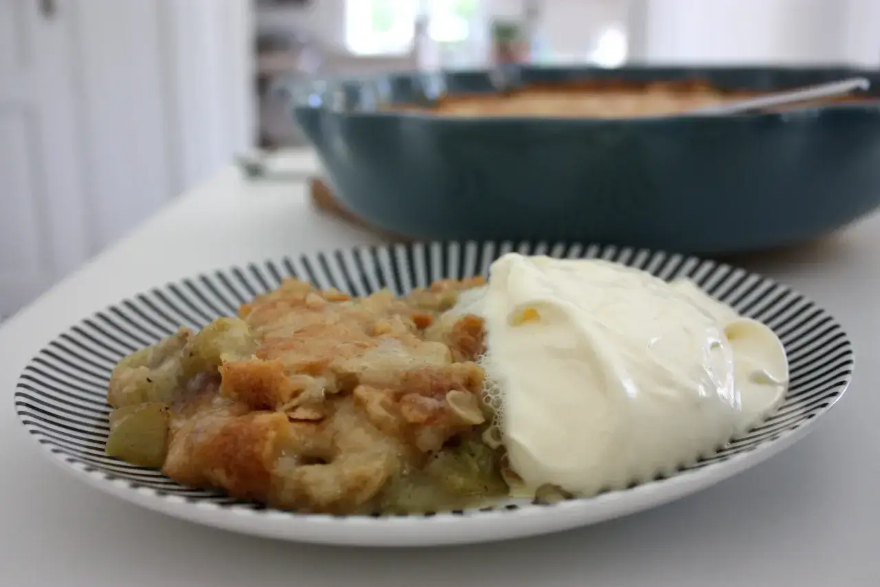 En portion rabarberpaj med kardemumma och en klick grädde på en randig tallrik.