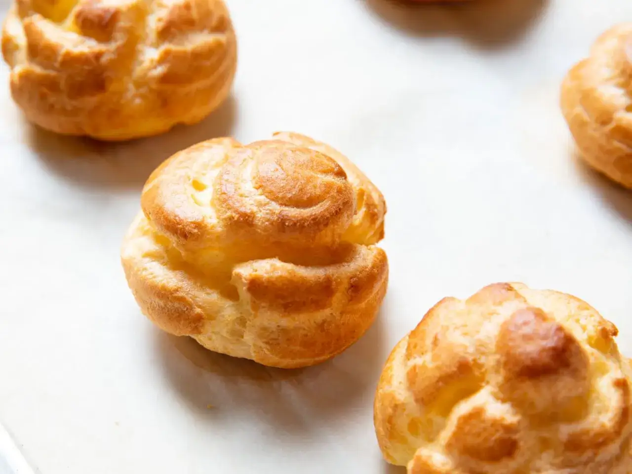 Gyldene, fluffiga petit choux-bakelser ligger utspridda på ett bakplåtspapper.