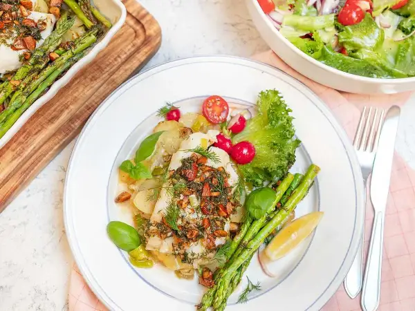 En portion torsk med citronsås, serverad med sparris, potatis och en fräsch sallad.