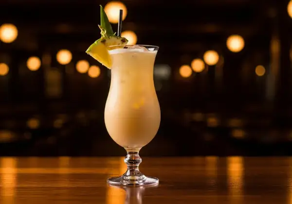 En krämig alkoholfri pina colada med ananasskiva och blad som dekoration, serverad i ett elegant glas på en träyta.