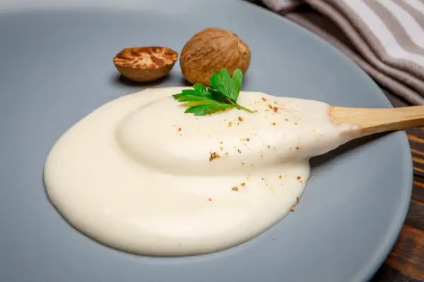 Krämig bechamelsås på en tallrik med muskotnötter och persilja. Perfekt för ditt bechamelsås recept.