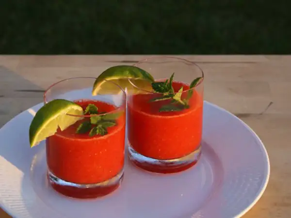 Två glas med fryst jordgubbsdaiquiri, garnerade med lime och mynta. Perfekt för ett somrigt strawberry daiquiri recept.