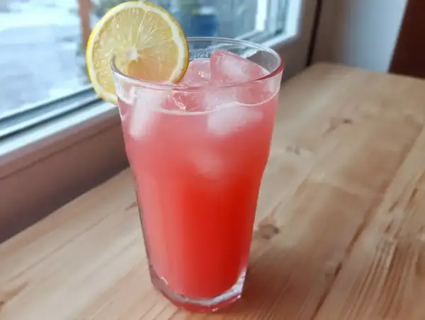 Ett glas rosa rabarberlemonad med is och en citronskiva, redo att avnjutas.