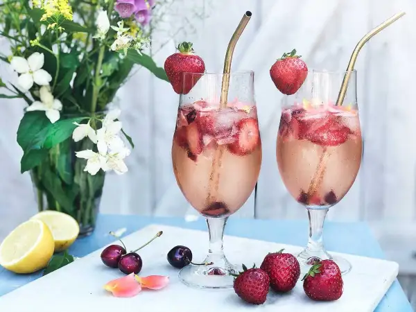Två glas med drink med gin och prosecco, fyllda med is, jordgubbar och körsbär. Garnerade med jordgubbar och serverade med citroner och blommor.