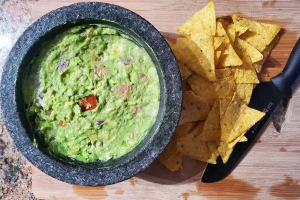 Närbild på en skål med hemgjord guacamole, perfekt för ett enkelt guacamole recept. Tortillachips och en kniv ligger bredvid.